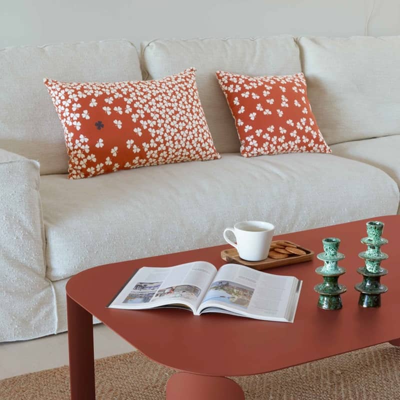 Auf einem schlicht gehaltenen Sofa liegen zwei farbige Kissen mit Kleebl&auml;ttern drauf
